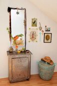 Zierquitten-Zweig in Glasvase auf antikem Metallschrank vor romantisch dekoriertem Wandspiegel, neben Bildergalerie, darunter afrikanischer Wäschekorb