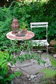 Alte Metalllaterne und Blumentopf auf Gartentisch mit Rost-Patina und schabloniertem Blumendekor, auf Boden mit Bruchsteinplatten und Kies