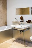 Minimalist washstand with metal frame against projecting wall and bathtub with metal cladding in bathroom with sand-coloured limestone floor