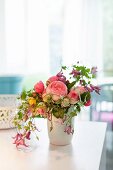 Blumenstrauss mit englischen Duftrosen und Clematis und anderen Blumensorten in weisser Vase auf Tisch