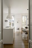 White kitchen counter in bright kitchen-dining room with floor-to-ceiling lattice windows, long dining table and designer chairs