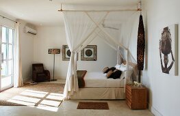 Canopied bed with mosquito nets in hotel room with sparse, African-style furnishings