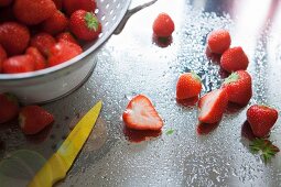 Freshly washed strawberries in a colander on a wet, stainless steel work surface