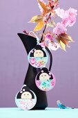 Hand-crafted, Japanese Kokeshi pendants on jug holding branches of cherry blossom