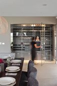 Set dining table and dining chairs with grey covers; woman walking into illuminated wine store behind glass doors