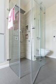 A floor-level, tiled shower cubicle with a rain shower and a hand-held shower head with a glass partition wall in a designer bathroom