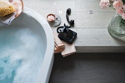 A partially visible bathtub next to an old-fashioned black telephone on a platform