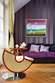 Designer armchair and side able in front of purple sofa and picture on striped wallpaper