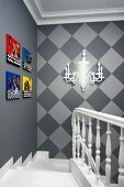 Head of staircase on elegant lantern with brightly coloured pictures and sconce lamp on walls in shades of grey