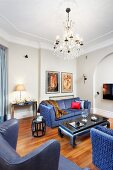 Blue sofa set and reading chair with blue leather cover around coffee table below chandelier in traditional living room