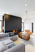 Grey corner sofa and wooden coffee table on animal-skin rug in front of partition wall with fire in integrated fireplace