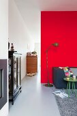 Retro standard lamp next to couch against partition wall covered in red felt; antique, glass-fronted cabinet to one side