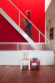Woman walking up metal staircase against red wall; red and white side tables against balustrade wall