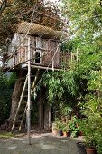 Verwunschenes Baumhaus aus vergrauten Holzbrettern mit Plexi-Vordach in einem Wohngarten
