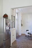 Notes stuck to stainless steel fridge with magnets, view into dining room with stucco ceiling, simple wooden floor and fitted display cabinets