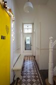 Bäuerliche Holzbank auf original Dielenfliesen in holländischem Wohnhaus; Geländerpfosten des alten Treppenaufgangs und gelb gestrichene Tür mit Schriftdeko