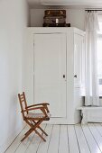 Vintage suitcases on original fitted wardrobe and wooden folding chair in bedroom with white wooden floor