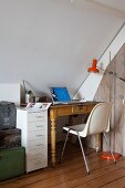 Kleine Schreibtischecke im Retro Stilmix unter Dachschräge: Antiktisch, Schalenstuhl und moderner Schubladencontainer neben Stapel alter Kisten