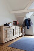 Rustic, plain wood sideboard in attic room; clothing hung from metal rod and stacked suitcases in background