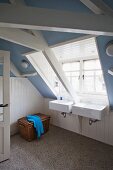 Attic bathroom with lavender-blue walls, white wainscoting and twin sinks below wide dormer window