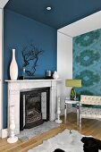 Ornaments on mantelpiece on blue wall; armchair and side table with chrome frame against accent wall with patterned wallpaper