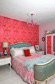 Rococo-style double bed and bedside tables in bedroom painted pale pink with deep pink, large-patterned wallpaper on accent wall