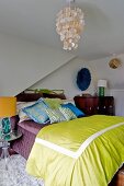 Capiz shell pendant lamp above bed with many scatter cushions and green bedspread in attic bedroom