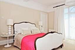 Pinkfarbene Tagesdecke auf weißem nostalgischem Französischem Bett mit geschwungenem Bettkopf- und Fussteil, Klassiker Nachttisch in elegantem, eklektischem Schlafzimmer