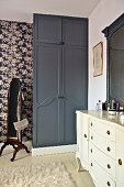 Bedroom with white dressing table and black fitted wardrobe against floral wallpaper