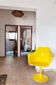 Yellow tulips chair in foyer with stone-flagged floor; view through open doors into bathroom and bedroom in background