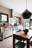 Vintage pendant lamp above dining table and metal chairs in front of kitchen counter with stainless steel cabinets