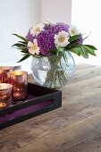 Glass tealight holders on tray and vase of flowers on rustic wooden table