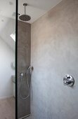 Regenbrause und Handbrause in begehbarer Dusche mit marmorierten Betonwänden und Glastrennwand