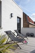 Two deckchairs on sunny, wooden roof terrace adjoining whitewashed brick façade