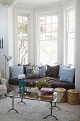 Window seat with many cushions in bay window behind glass coffee table on flokati rug