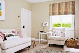 White couch and armchair in front of window with roller blind in living room