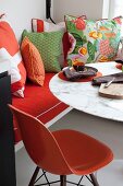 Orange, classic chair at marble-topped table and scatter cushions arranged on bench to one side