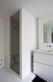 Ausschnitt eines Waschtisches mit weißem Unterschrank neben gemauertem Duschbereich und Glastür