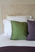 Kissen auf Bett mit weissen Bettbezügen vor beige marmoriertem Hintergrund
