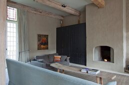 Graue Sofas und Bank mit roher Baumstammplatte als Couchtisch vor Kamin, seitlich ein Einbauschrank