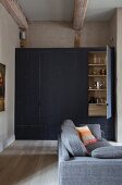 Fitted cupboard with board front in niche and grey sofa in foreground