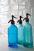 Old, blue glass soda siphons in front of white subway tiles