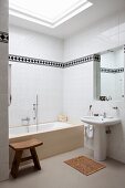 Wooden stool and wooden mat in bathroom with skylight; white tiles walls with black and white frieze