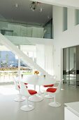 White Tulip table and matching chairs with red seat cushions in front of staircase in contemporary house