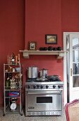 Stainless steel gas cooker against Bordeaux-red wall with masonry extractor hood in traditional kitchen
