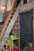 Holzleiter zur Galerieebene in Loftküche; Backsteinwand mit Industrietür aus schwarzem Metall