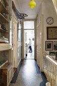 Narrow landing in traditional house with head of staircase to one side and woman in kitchen at far end