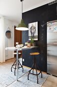 Vintage swivel stools and breakfast bar against black wall below pedant lamps with green metal lampshade
