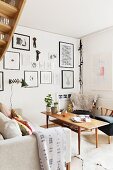 Wooden coffee table between fifties-style armchair and sofa in corner of living room; gallery of framed pictures on wall