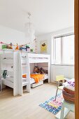 White bunk beds with ladder next to window in corner of children's bedroom; chair and section of table in foreground